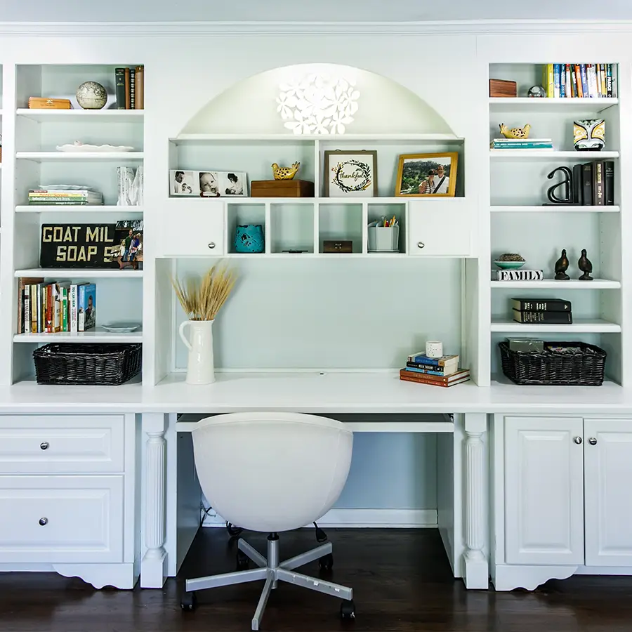 White home office with bookshelves, office cabinets, and desk chair.