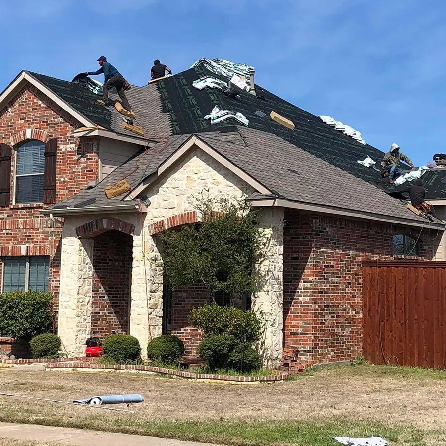Workers installing shingles on house roof